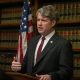 Man speaking at podium with American flag