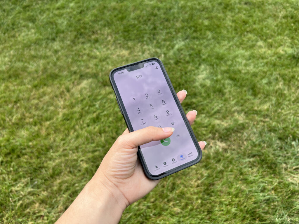 Hand holding smartphone dialing 911 outdoors