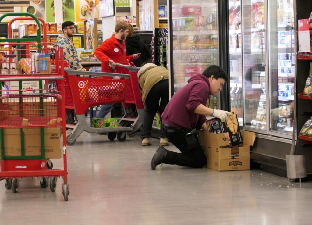 Employee stocking frozen food in grocery store aisle