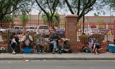 People sitting along sidewalk beside red fence