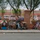 People sitting along sidewalk beside red fence