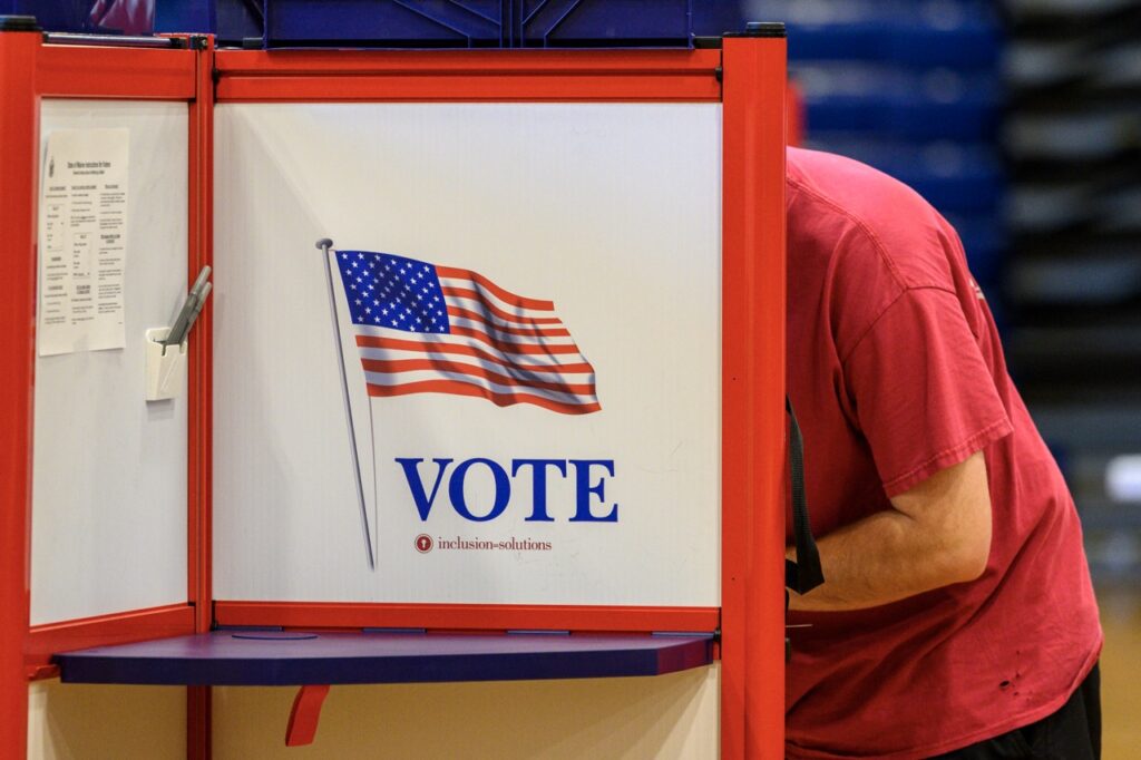 Person voting at booth with American flag