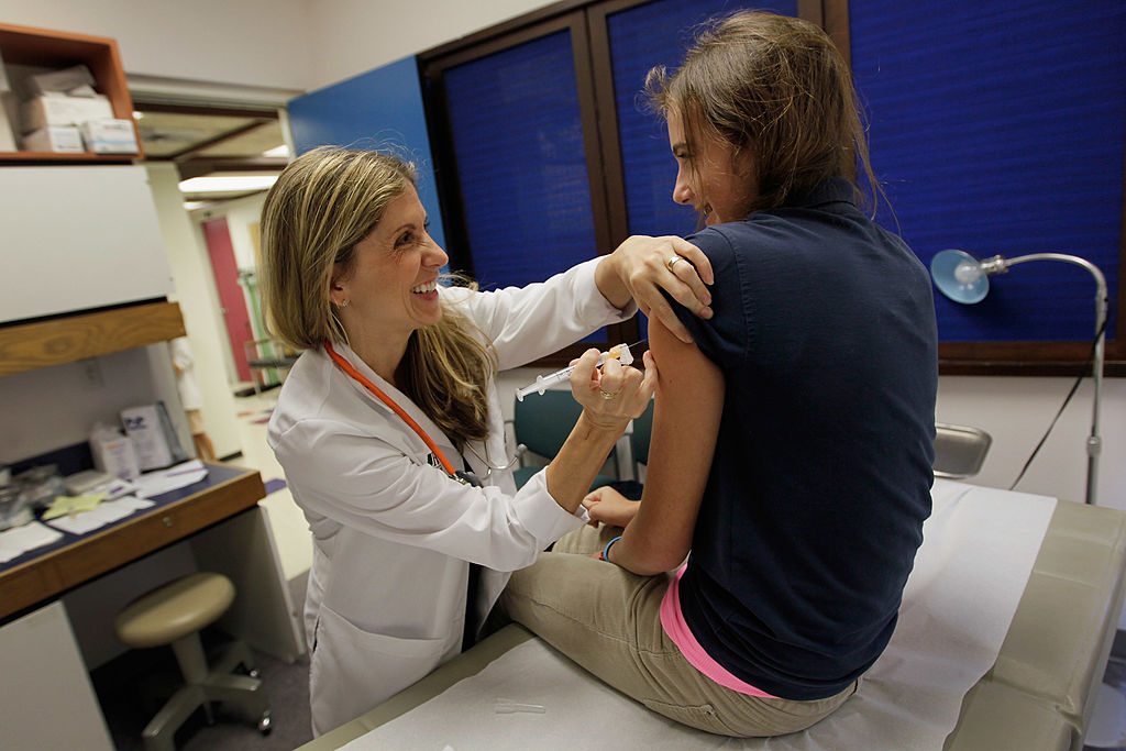 Doctor administering vaccine to teenage girl in clinic