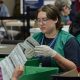 Election workers verify mail ballots in a counting facility, wearing gloves and green vests. — USPS mail ballot rules