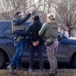 Law enforcement officers in tactical gear apprehending an individual near a police ve — sanctuary policies ICE enforcement