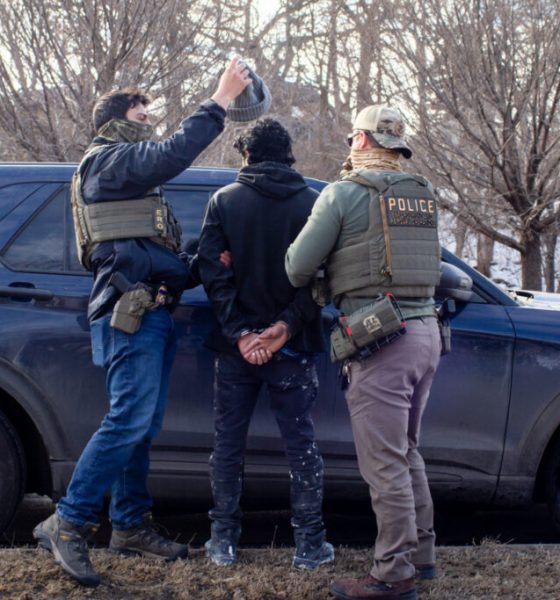 Law enforcement officers in tactical gear apprehending an individual near a police ve — sanctuary policies ICE enforcement