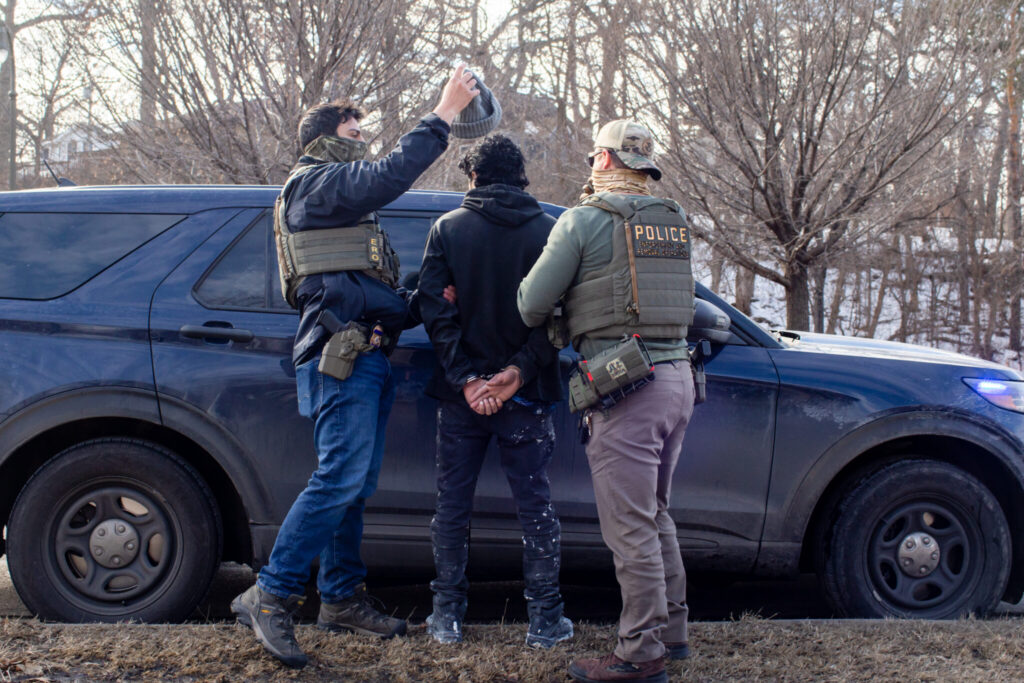 Law enforcement officers in tactical gear apprehending an individual near a police ve — sanctuary policies ICE enforcement