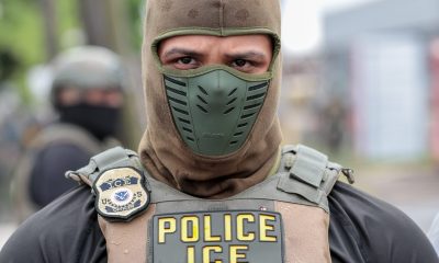 An ICE officer in tactical gear with a mask, displaying a badge and the word 'POLICE' on his — ICE monthly arrests record