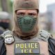 An ICE officer in tactical gear with a mask, displaying a badge and the word 'POLICE' on his — ICE monthly arrests record