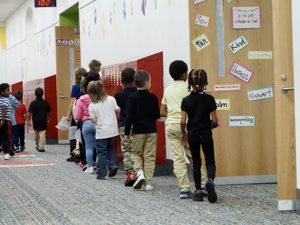 Children walking in a school hallway, passing by colorful educational posters and lock — federal education funding waivers