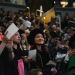 Graduates in caps and gowns celebrating at a commencement ceremony, with a crowd in the backg — DHS H-1B visa fee proposal