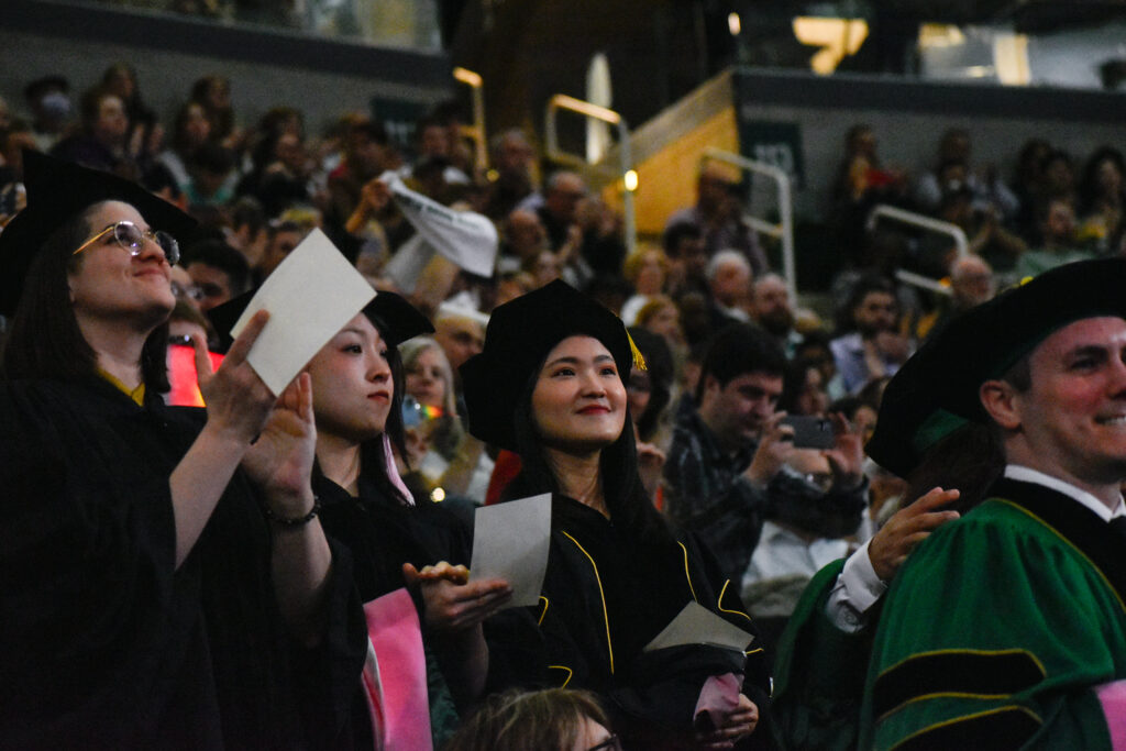Graduates in caps and gowns celebrating at a commencement ceremony, with a crowd in the backg — DHS H-1B visa fee proposal