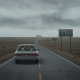 A car drives down a long, empty road towards a distant hospital sign, highlighting challenges in rural maternity care access.
