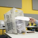 A hand placing mail-in ballots into a USPS ballot box at a voting site, with a bright yell — Supreme Court mail-in ballots