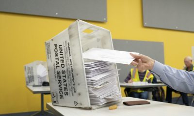 A hand placing mail-in ballots into a USPS ballot box at a voting site, with a bright yell — Supreme Court mail-in ballots