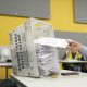 A hand placing mail-in ballots into a USPS ballot box at a voting site, with a bright yell — Supreme Court mail-in ballots