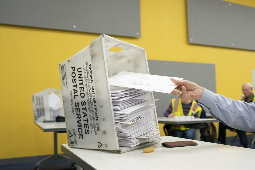 A hand placing mail-in ballots into a USPS ballot box at a voting site, with a bright yell — Supreme Court mail-in ballots