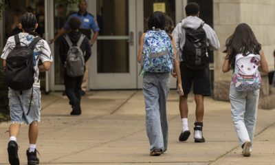Students walking towards a school entrance, carrying backpacks, highlighting the issue of public school closures.