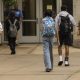 Students walking towards a school entrance, carrying backpacks, highlighting the issue of public school closures.