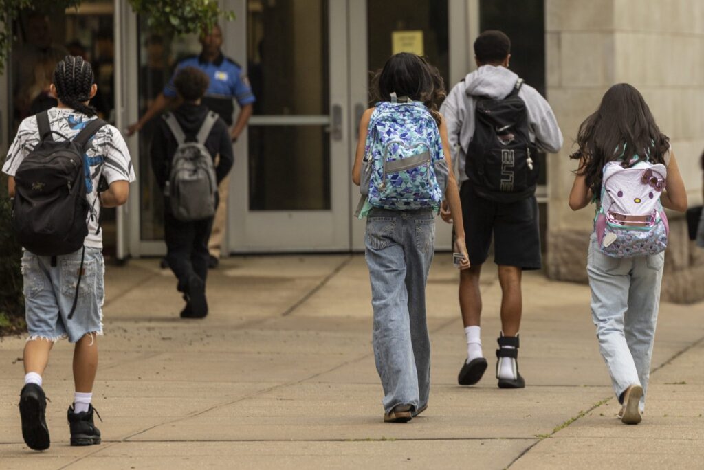 Students walking towards a school entrance, carrying backpacks, highlighting the issue of public school closures.