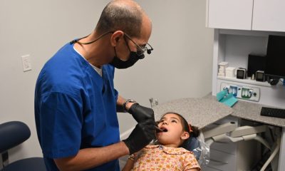 A pediatric dentist examines a young girl in a dental office, highlighting immigrant children healthcare challenges.