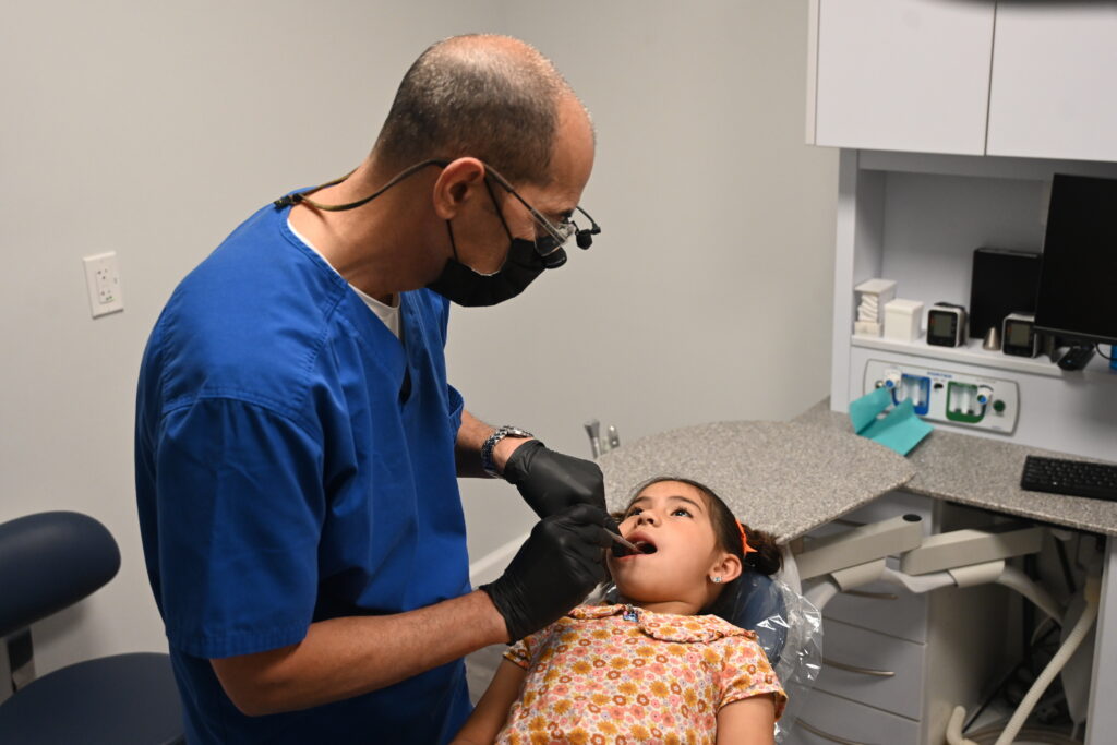 A pediatric dentist examines a young girl in a dental office, highlighting immigrant children healthcare challenges.