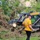Two women discuss cleanup efforts near a tree debris pile and heavy machinery after a storm, highlighting FEMA disaster aid.