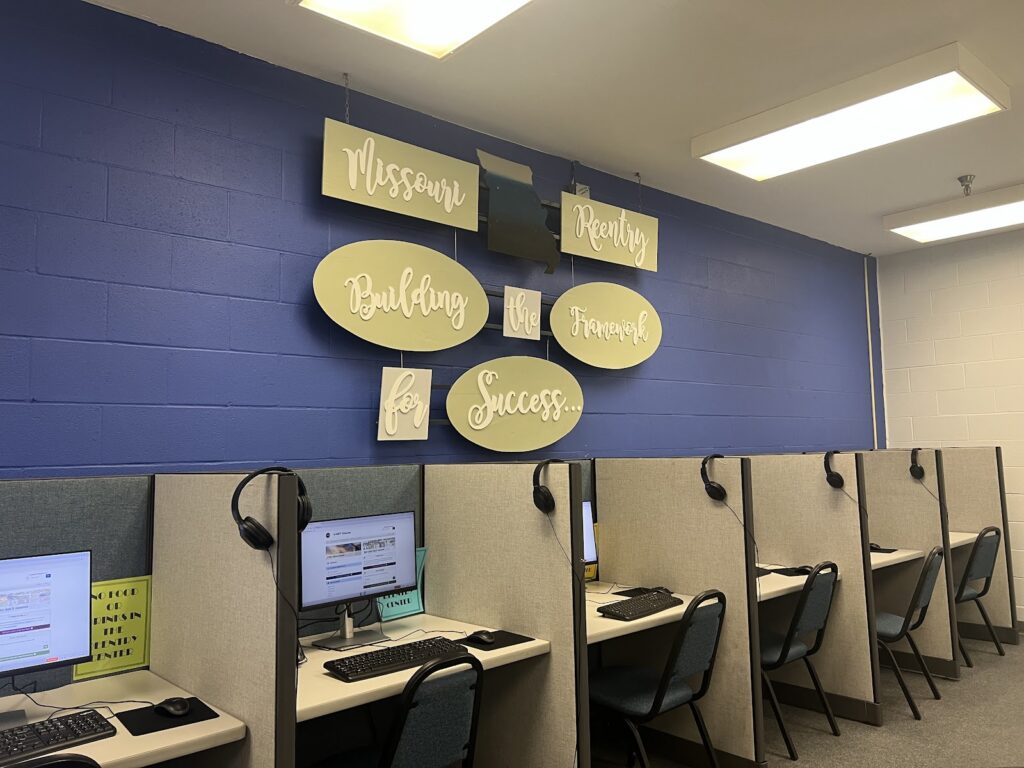 A room with computer workstations and a wall sign reading 'Missouri Reentry Framework for — women on parole mental health