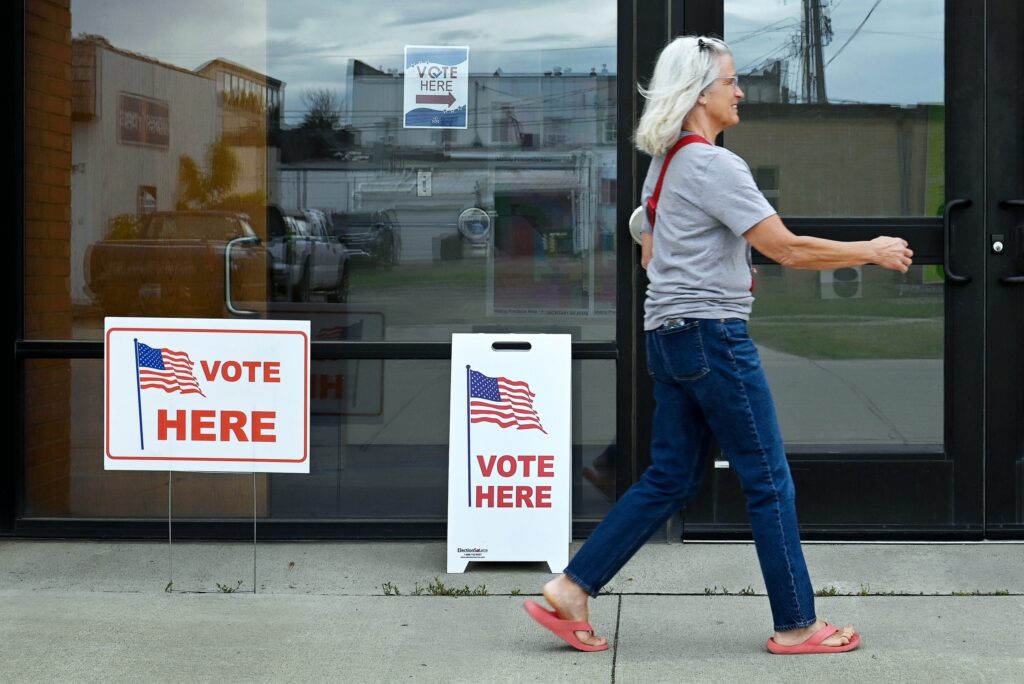 A woman walks past polling signs that say 'Vote Here' outside a voting location. — can trump send troops to polling places