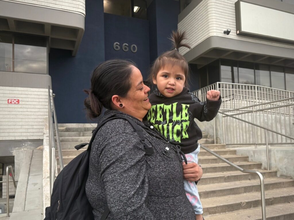 A woman holds a young child outside a building, both smiling, with the number 660 visib — Trump Public Charge Rule Lawsuit