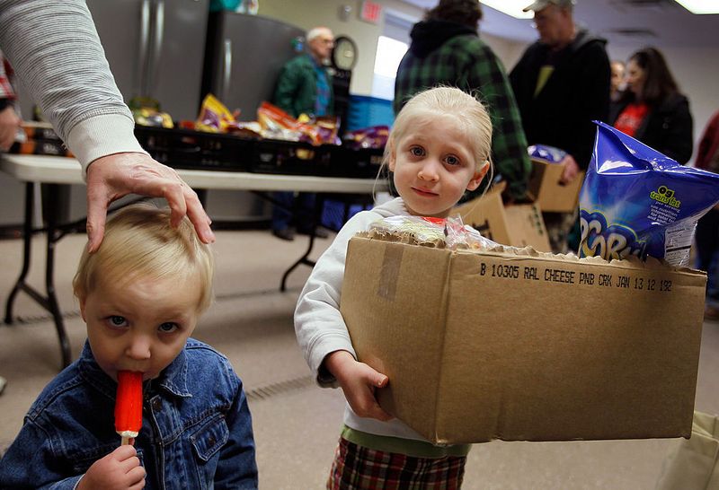 Two children at a food distribution event, one holding a box of snacks and the other with a popsicle. — us poverty rate
