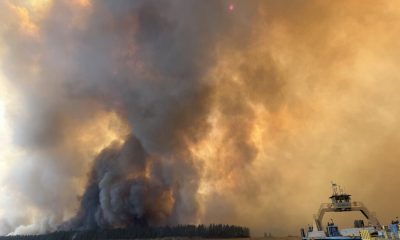 Smoke and flames rise from a wildfire near the Colville Reservation, with a boat in the f — Colville Reservation Wildfires