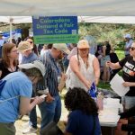A diverse group of people gathers under a tent to discuss state tax ballot measures, incl — state tax ballot measures 2024