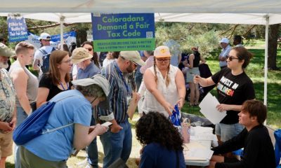 A diverse group of people gathers under a tent to discuss state tax ballot measures, incl — state tax ballot measures 2024