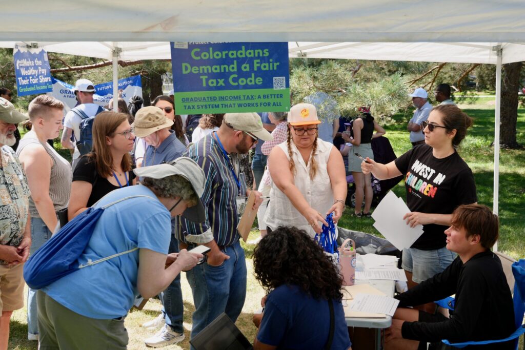 A diverse group of people gathers under a tent to discuss state tax ballot measures, incl — state tax ballot measures 2024