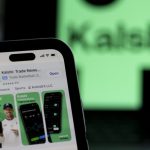 Utah Sues Kalshi: a phone displays the Kalshi trading app against a blurred green Kalshi sign.