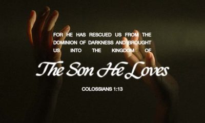 Colossians 1 13 daily bible verse over raised hands in a dark, softly lit scene