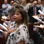 New citizens stand with hands over their hearts and American flags during a n — Trump administration naturalization delays