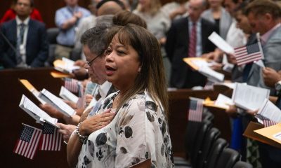 New citizens stand with hands over their hearts and American flags during a n — Trump administration naturalization delays