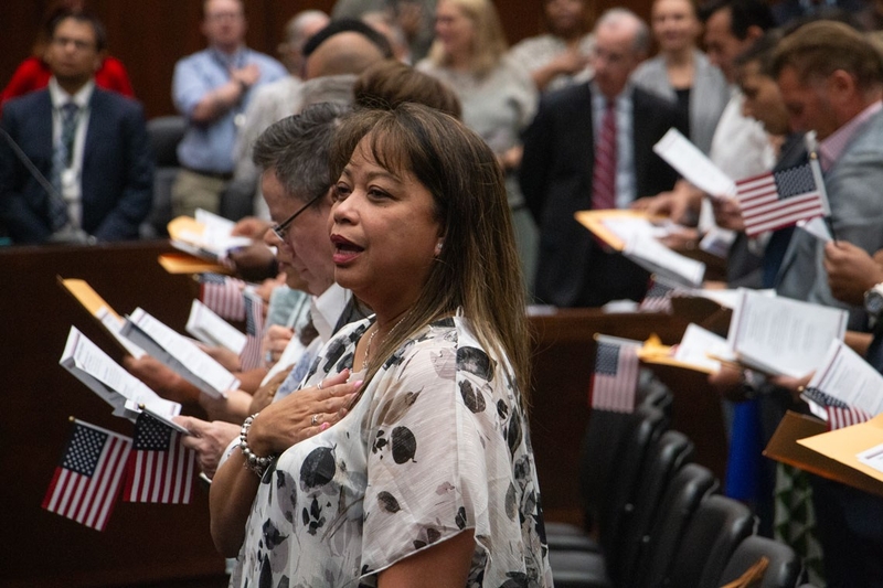 New citizens stand with hands over their hearts and American flags during a n — Trump administration naturalization delays