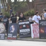 Protesters hold anti-abortion signs along a sidewalk, including posters showing fetal — pregnancy criminal charges report