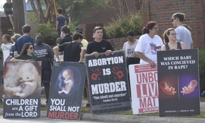Protesters hold anti-abortion signs along a sidewalk, including posters showing fetal — pregnancy criminal charges report