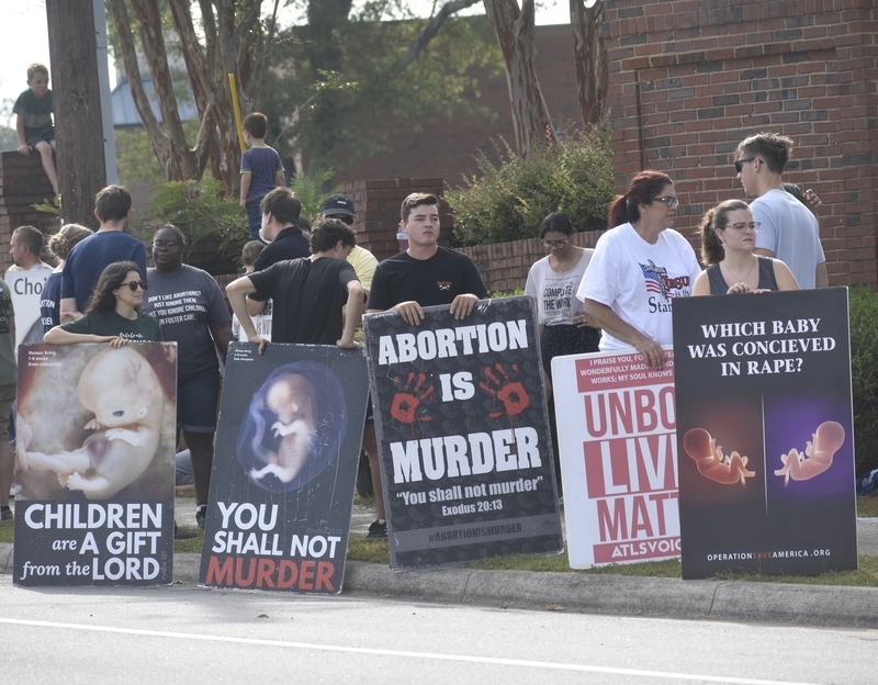 Protesters hold anti-abortion signs along a sidewalk, including posters showing fetal — pregnancy criminal charges report