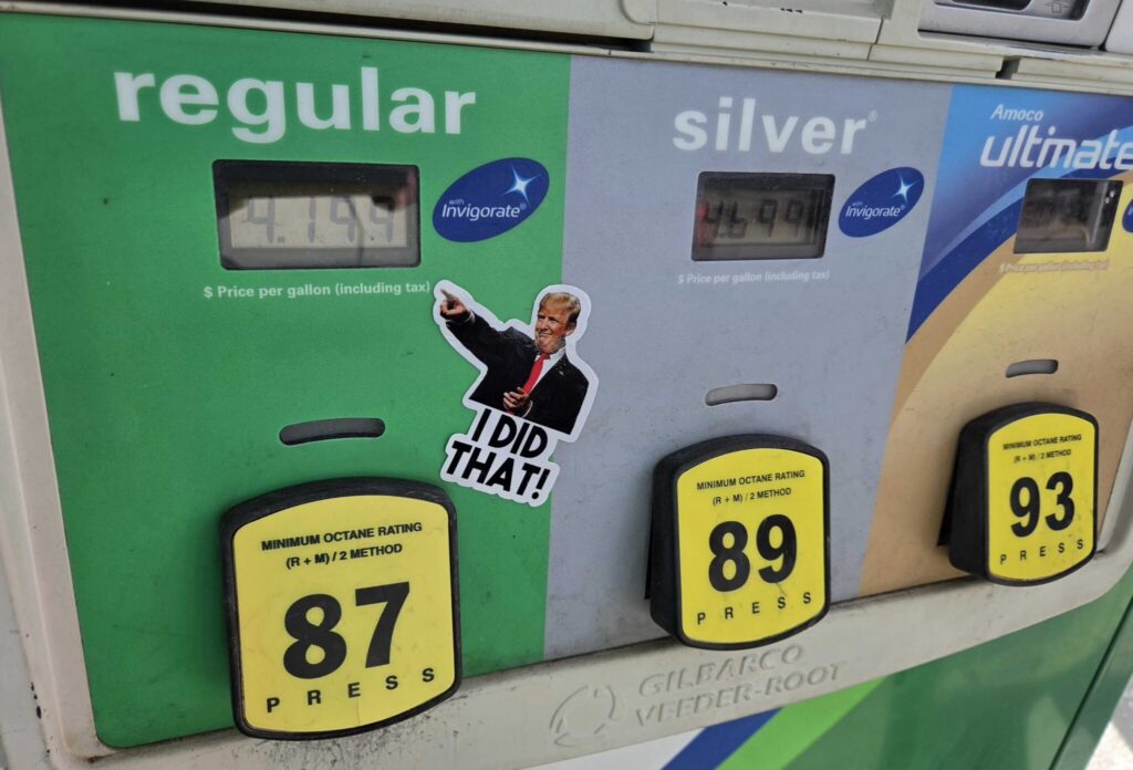 Gas pump displaying fuel prices with a sticker featuring a thumbs-up gesture and text referenc — States Suspending Gas Tax