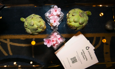 Artichokes, pink flowers, and an Artichoke Credit Union business card arranged on a reflective table.