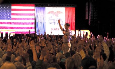 A crowd raises their hands in support during a political rally, with flags in the background — Democrats governor majority