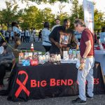 A community event table displaying HIV prevention materials and resources, with people engag — HIV prevention funding cuts