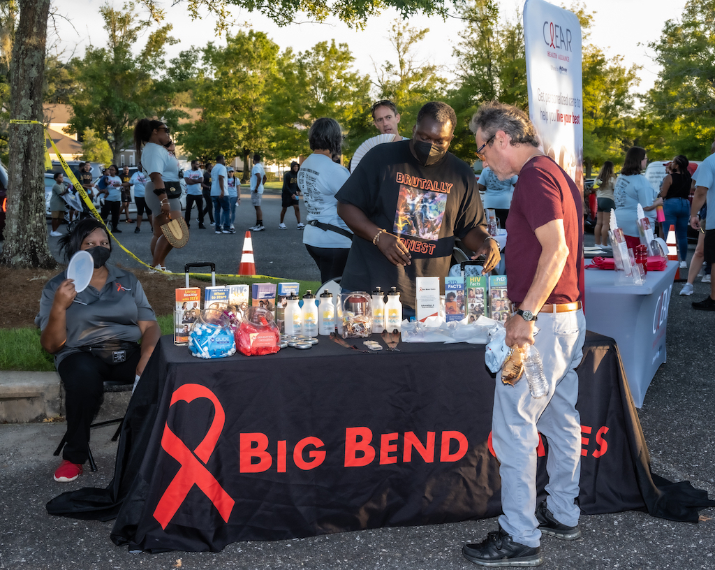 A community event table displaying HIV prevention materials and resources, with people engag — HIV prevention funding cuts