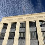 Facade of a county courthouse with a flag and blue sky in the background, — District Attorney Elections Prison Admissions
