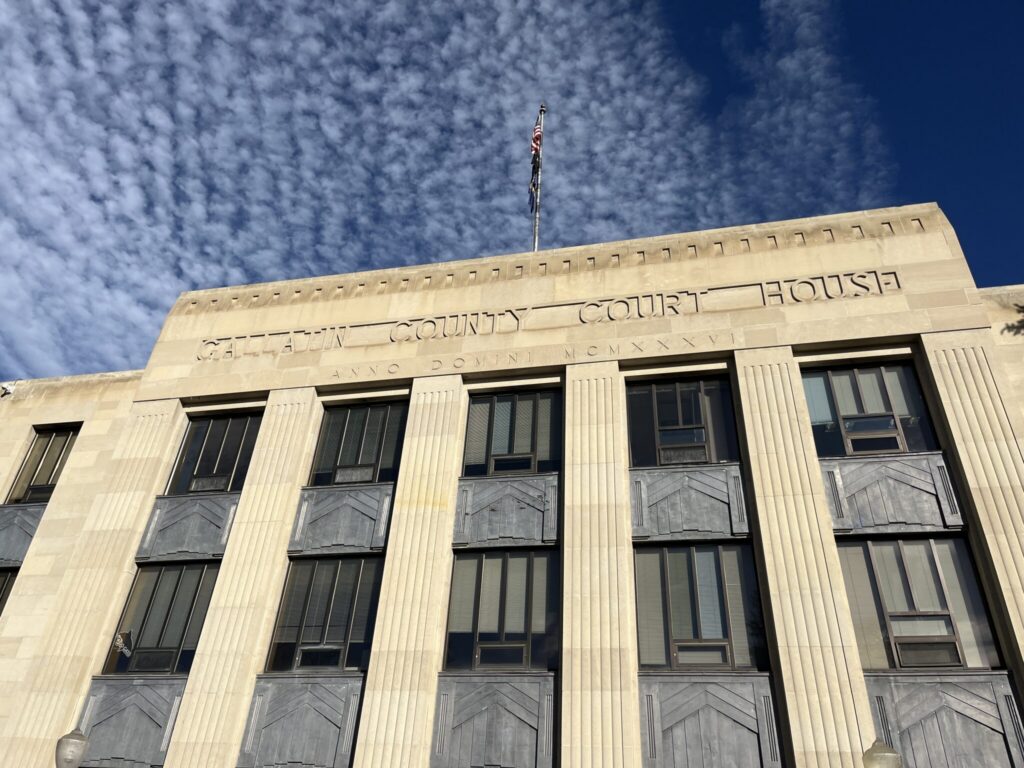 Facade of a county courthouse with a flag and blue sky in the background, — District Attorney Elections Prison Admissions